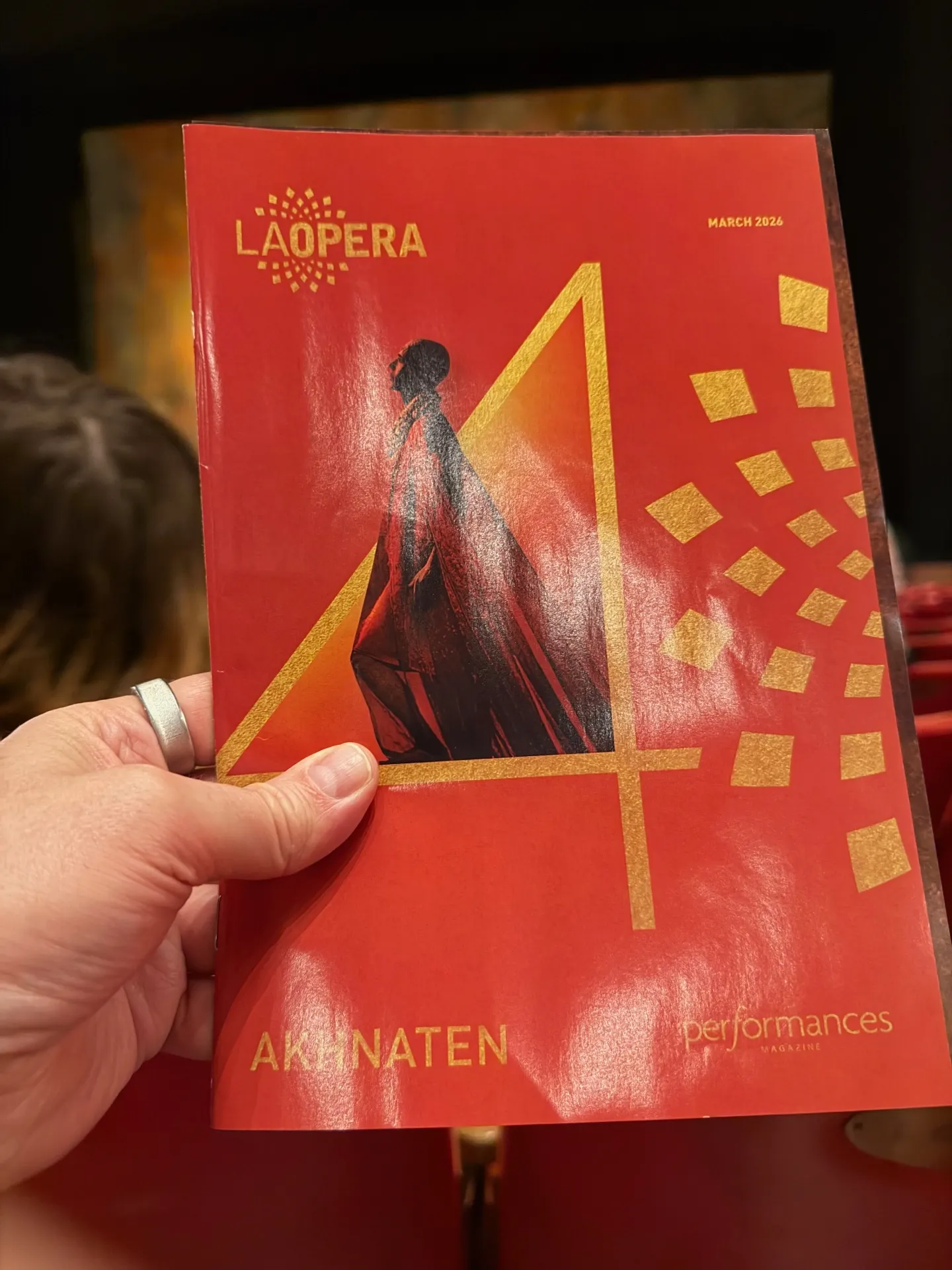 LA Opera Performances magazine for Akhnaten, March 2026, held up in the house with a red cover, gold geometric foil, and a silhouetted pharaoh figure