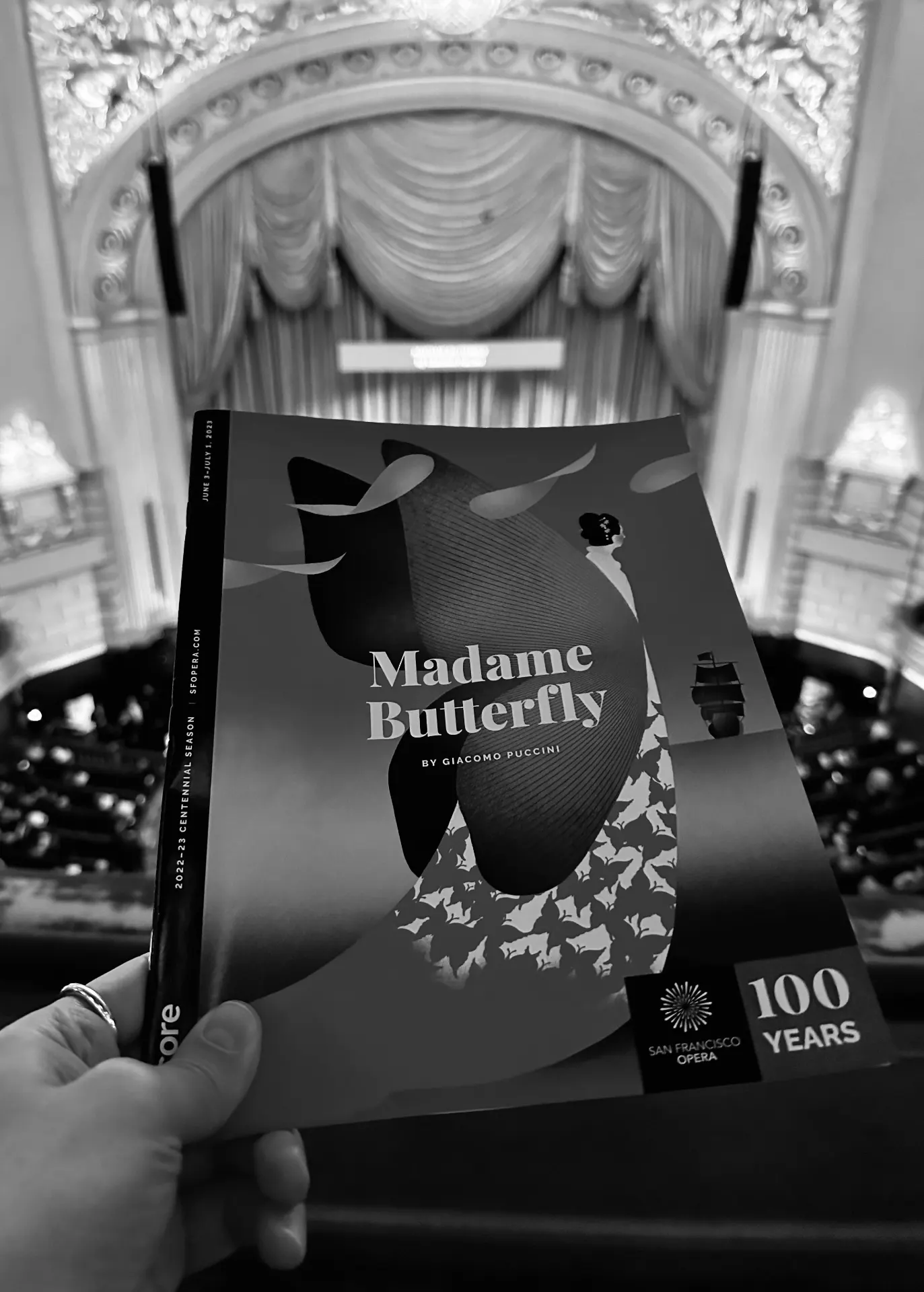 Black and white photograph of a Madame Butterfly program held up against the gilded War Memorial proscenium and house curtain