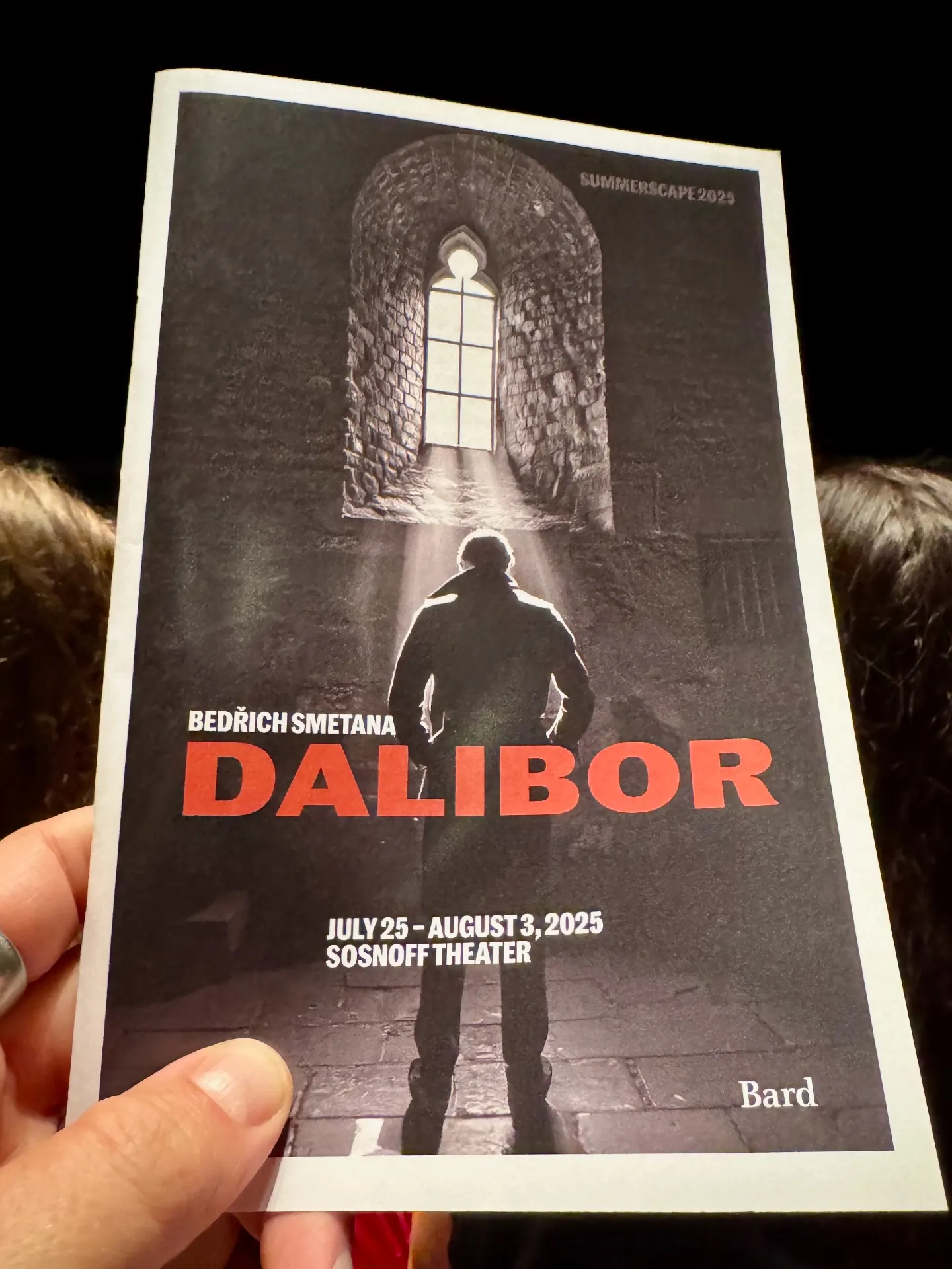 Bard SummerScape 2025 program for Smetana's Dalibor held up in the house, cover showing a silhouetted figure under a barred prison window