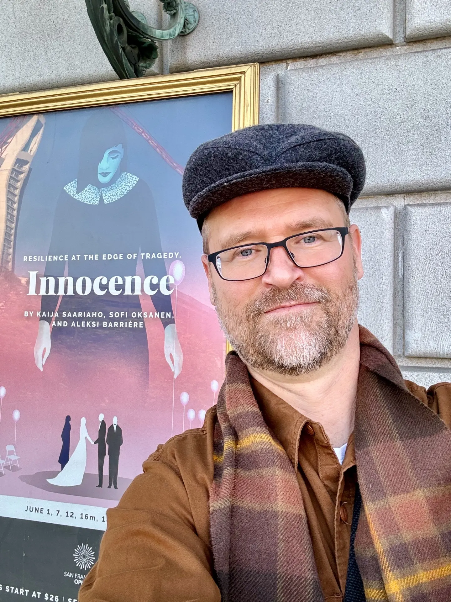 Self-portrait in a wool cap and flannel shirt outside the SF Opera house, beside the framed Innocence poster