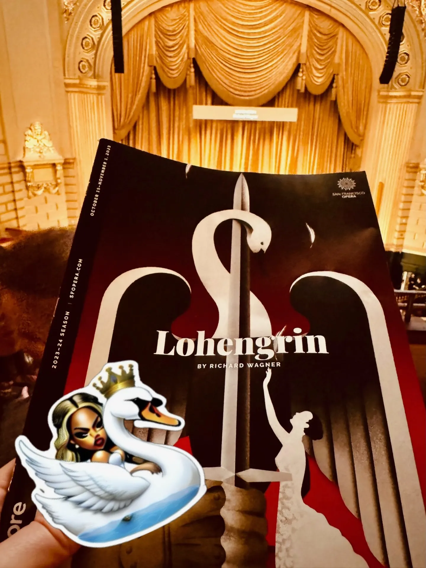 Lohengrin program with a swan-and-sword cover, held in front of the War Memorial curtain, a Beyoncé-as-swan sticker in the corner