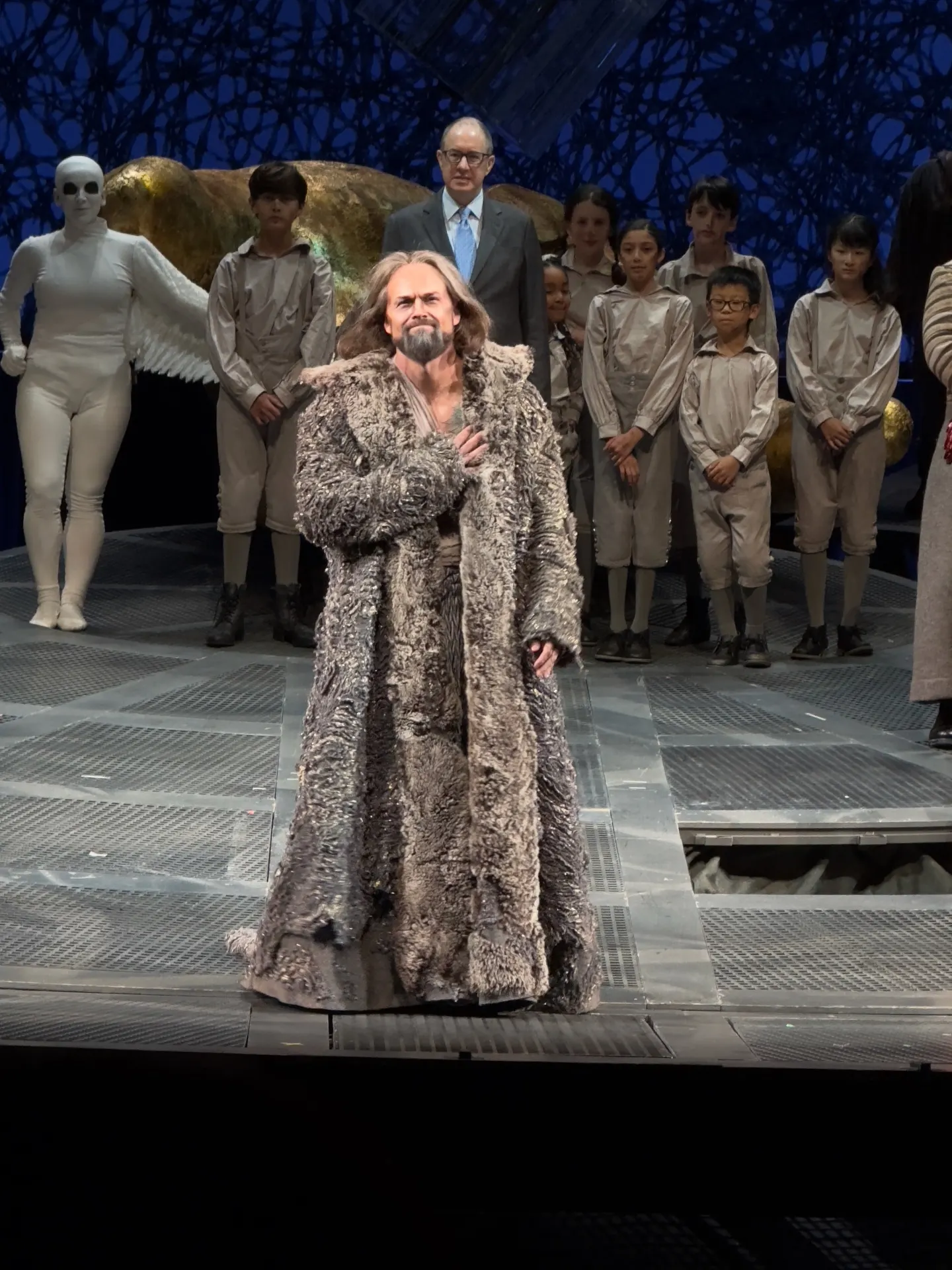 Solo curtain-call bow of bass-baritone Gurnemanz in a long fur coat, hand to chest, children's chorus and an angelic white-suited figure behind