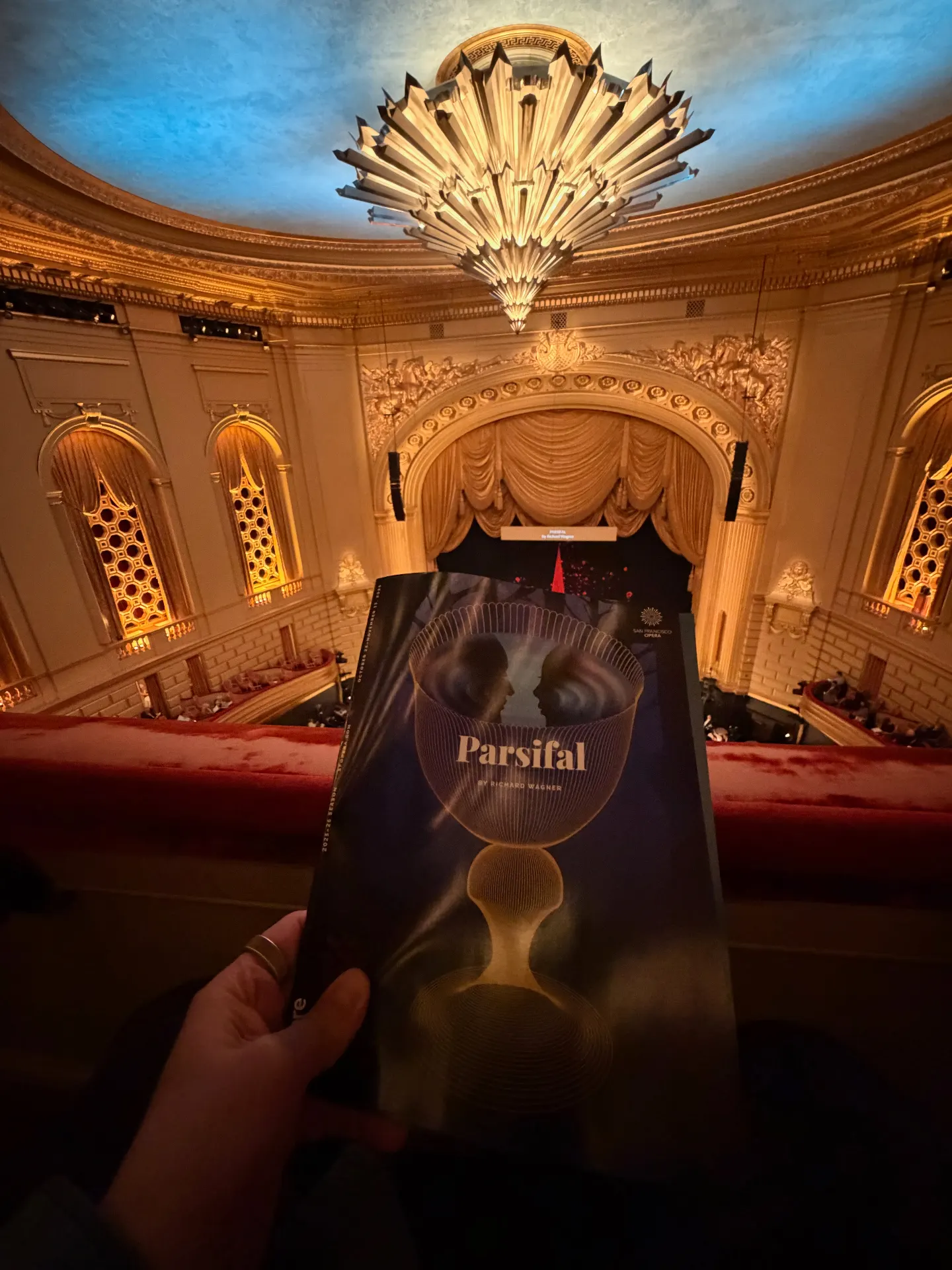 Parsifal program held up from a balcony seat at the War Memorial Opera House, the gilded proscenium and starburst chandelier filling the frame above