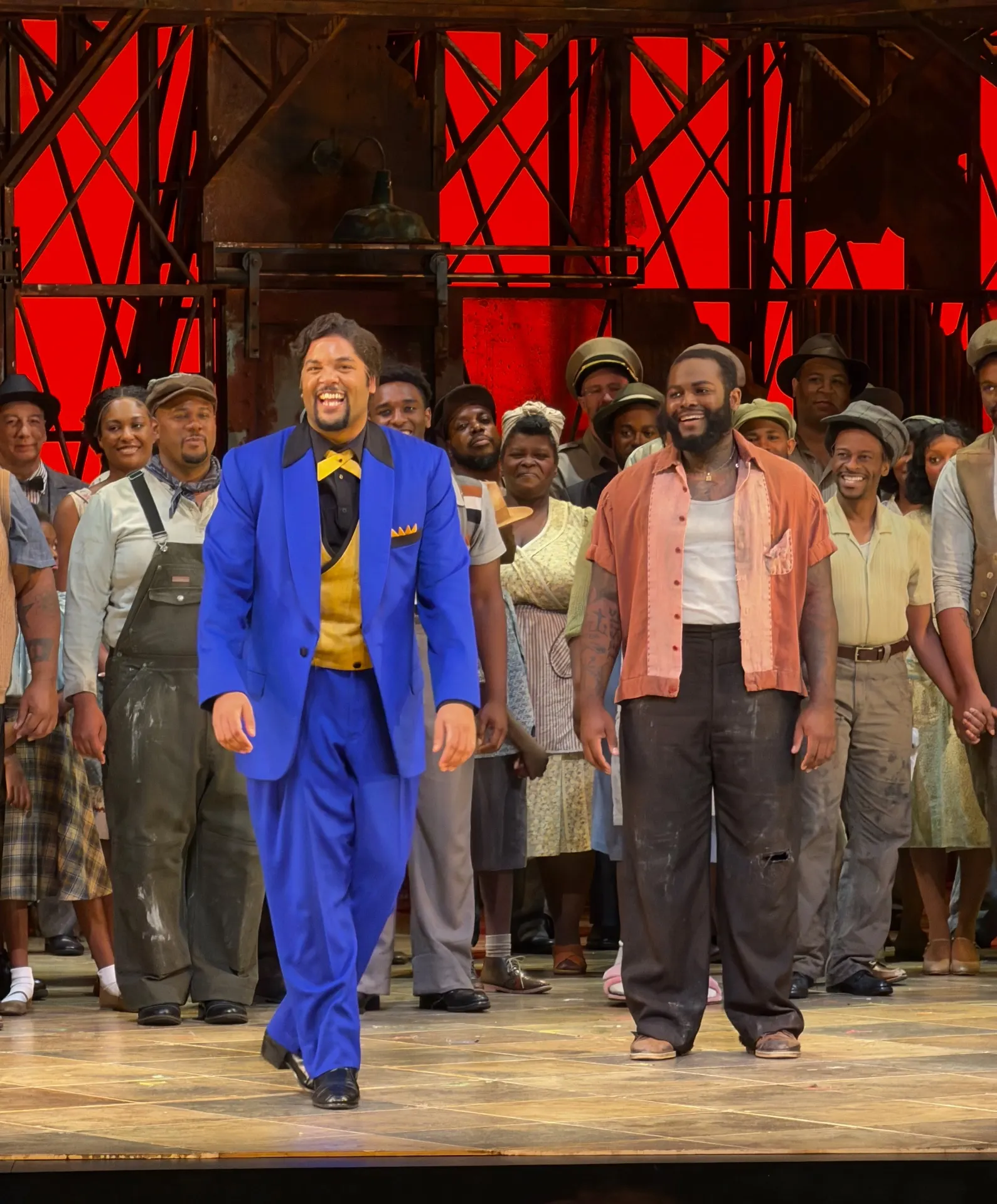 Sportin' Life taking a solo bow in an electric blue suit and gold waistcoat, Crown beside him in salmon shirt, Catfish Row chorus behind under a red sky