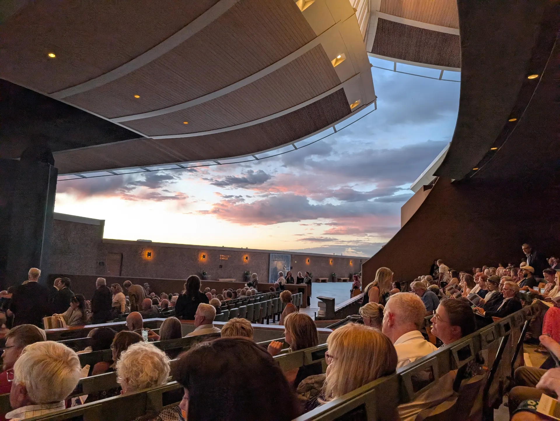 Interior of the Crosby Theatre at Santa Fe Opera with the audience settling in, the open back of the house framing a pink-and-blue desert sunset
