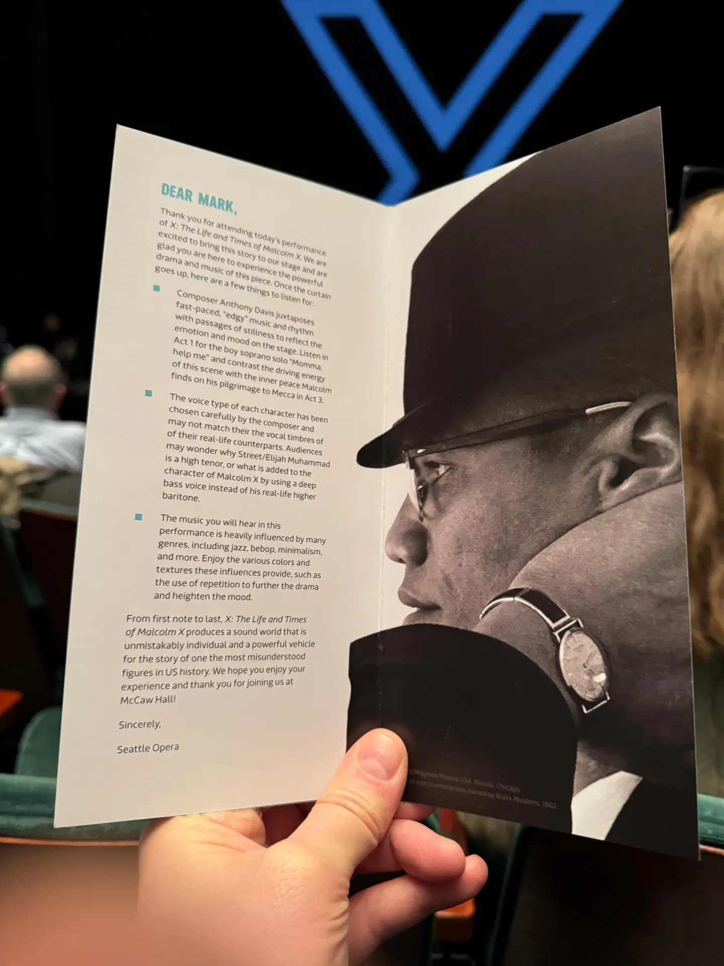 Seattle Opera audience welcome card opened to 'Dear Mark,' with Malcolm X in profile on the right page, blue lobby chevrons behind