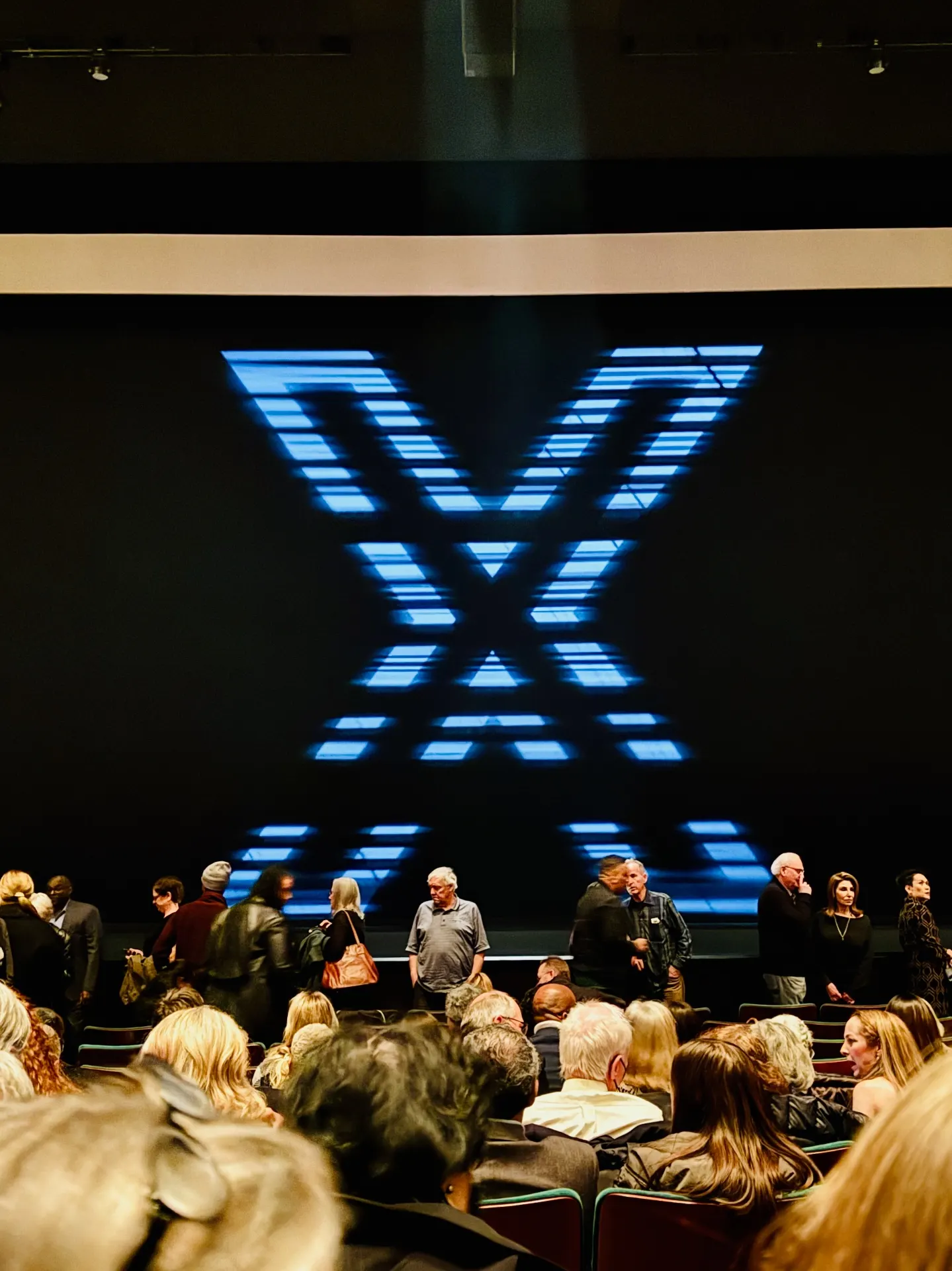 Pre-show projection of a pixelated blue X on the McCaw Hall curtain, audience filing in
