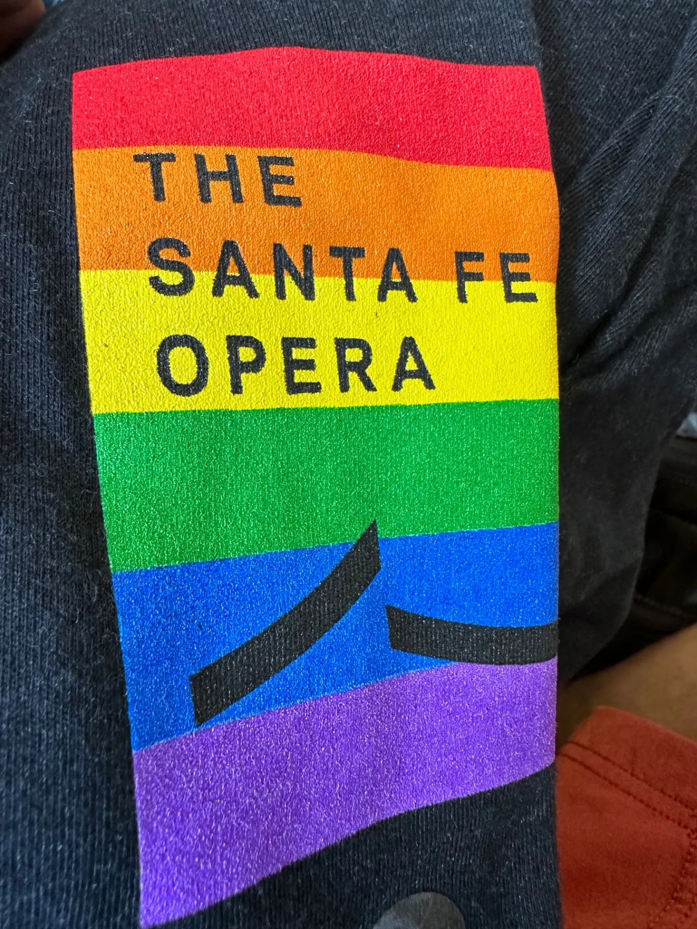 Close-up of a Santa Fe Opera Pride t-shirt with the company logo printed across rainbow stripes