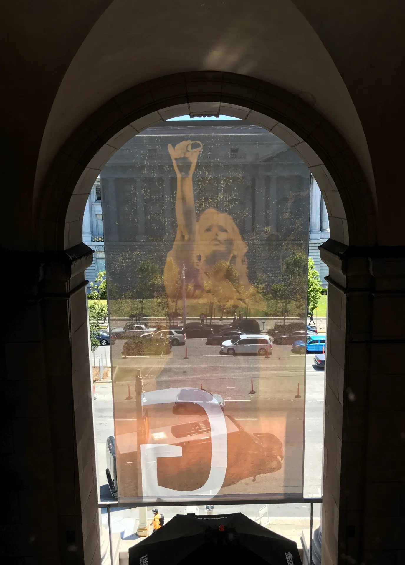 Translucent opera scrim with a singer's portrait, seen through an arched window with City Hall behind