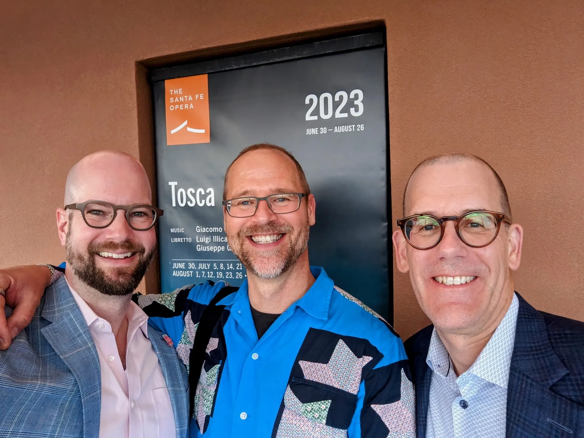 Three friends smiling in front of a Santa Fe Opera Tosca poster for the 2023 season