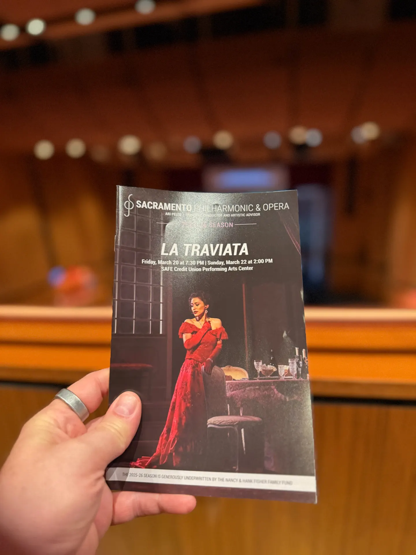 Sacramento Philharmonic & Opera La Traviata program held up in the hall, cover shows Violetta in a red gown beside a candlelit table