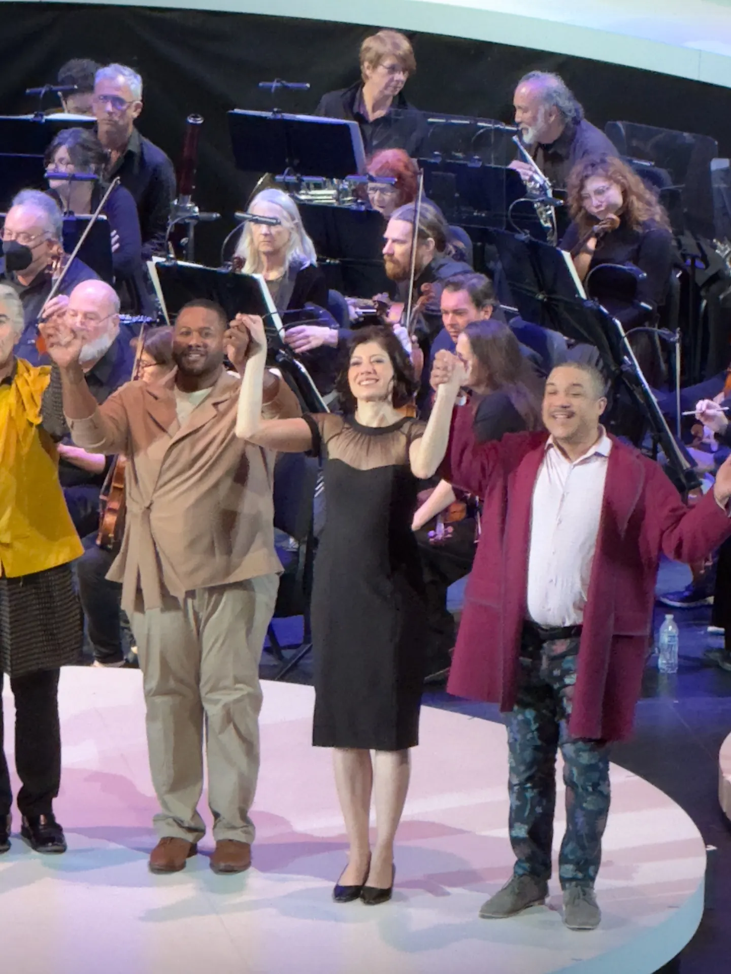 Principals of X joining hands at curtain call in front of the seated orchestra, smiling broadly